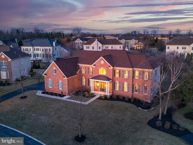 colonial house featuring brick siding, a residential view, a shingled roof, and a front yard