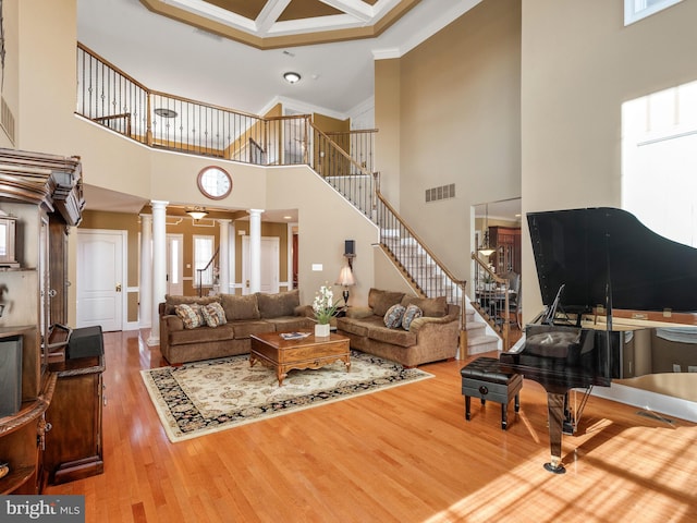 living area featuring stairway, wood finished floors, visible vents, ornate columns, and ornamental molding