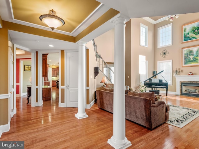 living room featuring ceiling fan, stairway, ornamental molding, decorative columns, and light wood-style floors