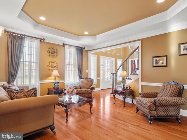 living area with a raised ceiling, a healthy amount of sunlight, light wood-style flooring, and crown molding