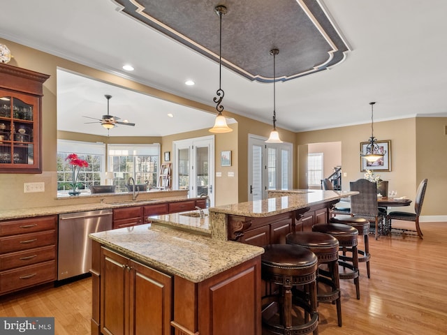 kitchen with a breakfast bar, light wood-type flooring, ornamental molding, stainless steel dishwasher, and a sink