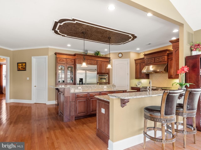 kitchen featuring a breakfast bar, an island with sink, stainless steel appliances, under cabinet range hood, and light wood-type flooring