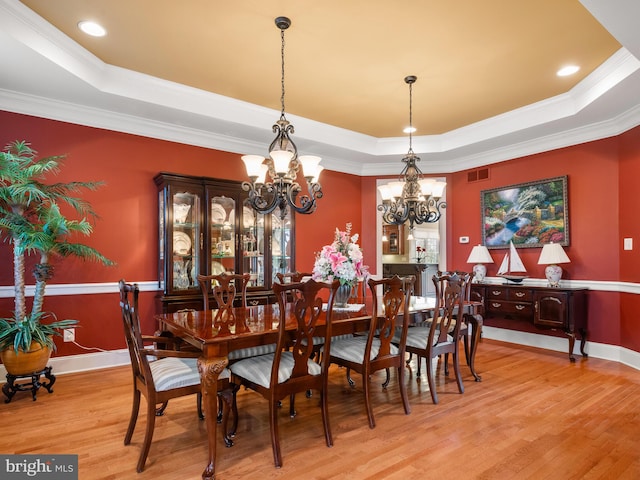 dining room featuring visible vents, baseboards, light wood-style floors, a notable chandelier, and a raised ceiling