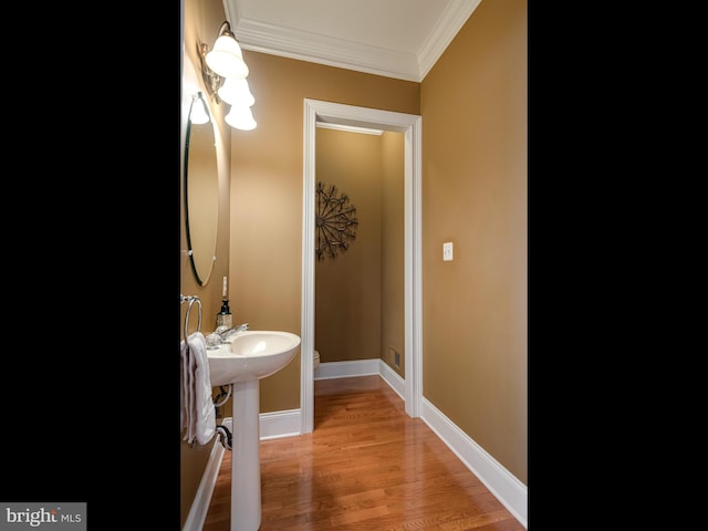 half bath featuring toilet, crown molding, baseboards, and wood finished floors