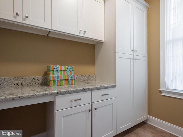 kitchen with white cabinets, light stone countertops, and baseboards