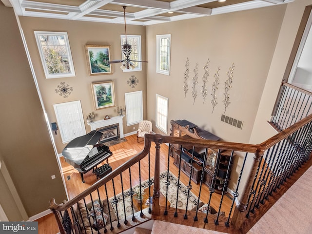 staircase with visible vents, beamed ceiling, a fireplace with flush hearth, wood finished floors, and coffered ceiling