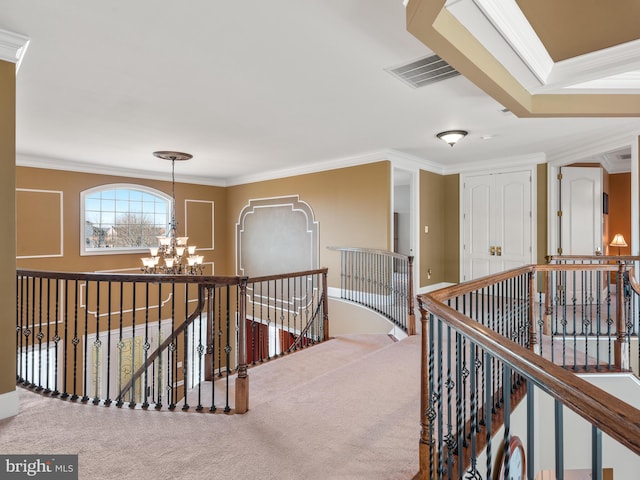 hall with visible vents, carpet floors, an upstairs landing, ornamental molding, and an inviting chandelier