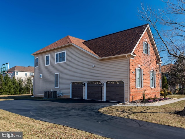 view of property exterior with aphalt driveway, central AC unit, an attached garage, and a shingled roof