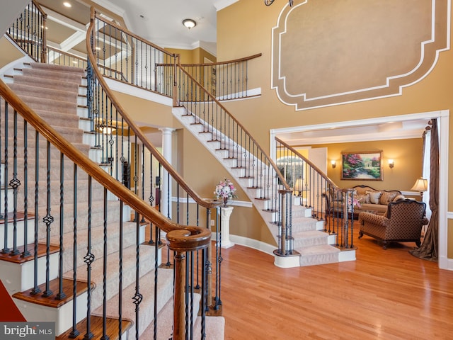 stairway featuring baseboards, a high ceiling, wood finished floors, and crown molding