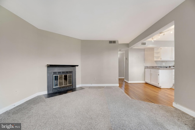 unfurnished living room featuring a fireplace with flush hearth, light colored carpet, baseboards, and visible vents