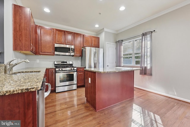 kitchen with light wood finished floors, ornamental molding, appliances with stainless steel finishes, and a sink