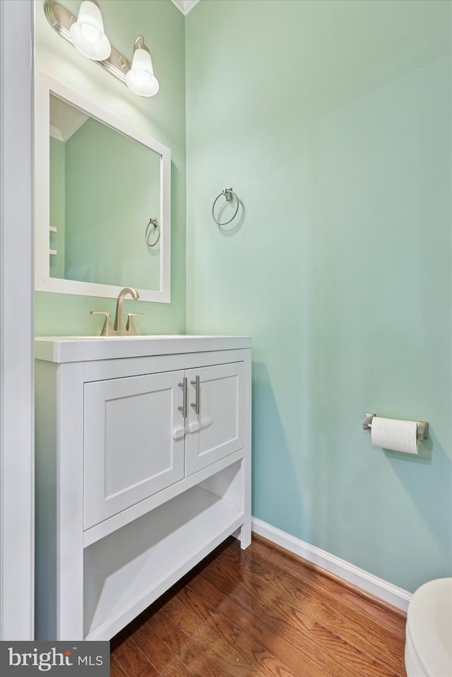 bathroom featuring baseboards, toilet, wood finished floors, and vanity