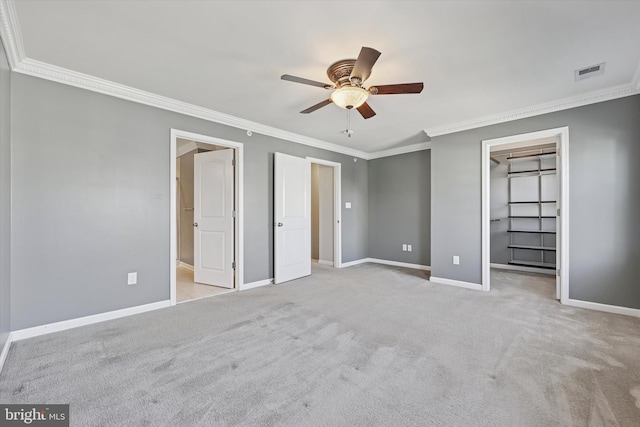 unfurnished bedroom featuring visible vents, a walk in closet, carpet floors, crown molding, and baseboards