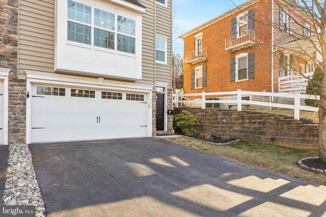 exterior space featuring an attached garage, fence, stone siding, and driveway