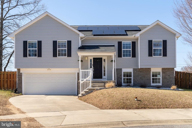 raised ranch with fence, concrete driveway, a garage, brick siding, and solar panels