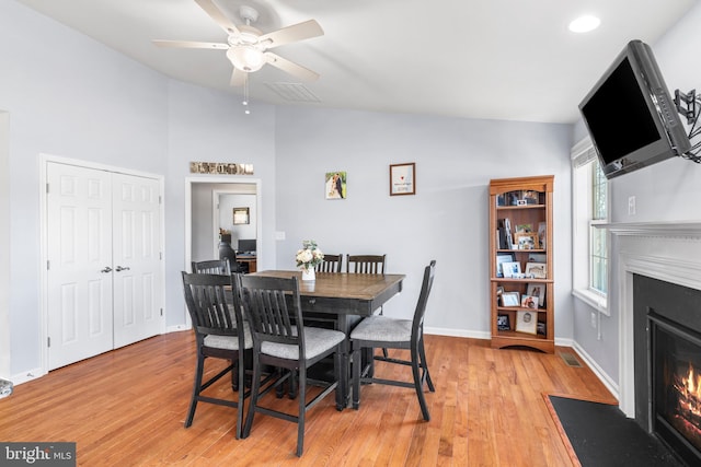 dining room with visible vents, a fireplace with flush hearth, lofted ceiling, light wood-style flooring, and baseboards