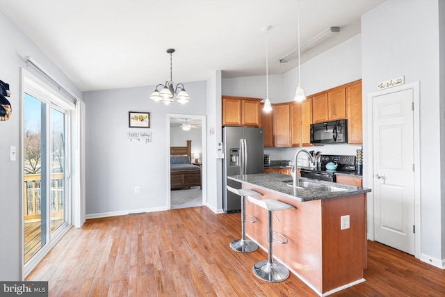 kitchen with a center island with sink, a kitchen bar, light wood-style flooring, hanging light fixtures, and black appliances