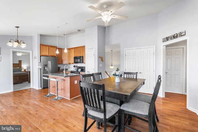 dining area featuring baseboards, light wood-style flooring, a towering ceiling, and ceiling fan with notable chandelier