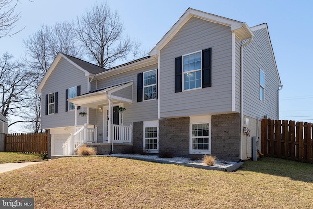 split foyer home with stone siding, a garage, a front lawn, and fence