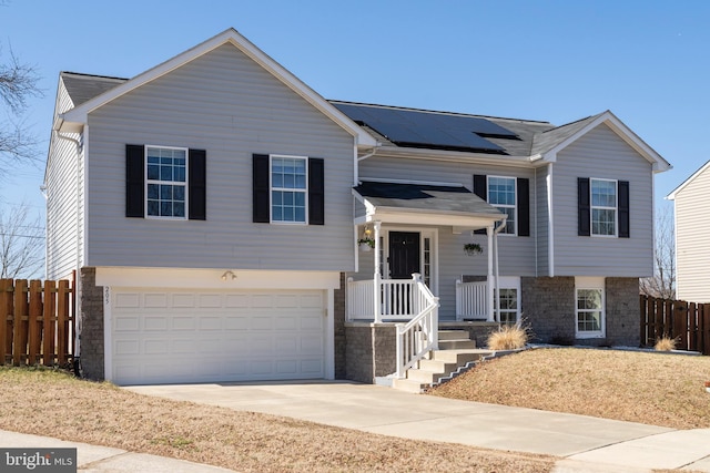 bi-level home with an attached garage, fence, stone siding, and roof mounted solar panels