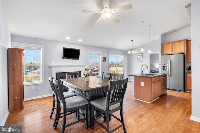 dining room with plenty of natural light, a fireplace, light wood-type flooring, and baseboards