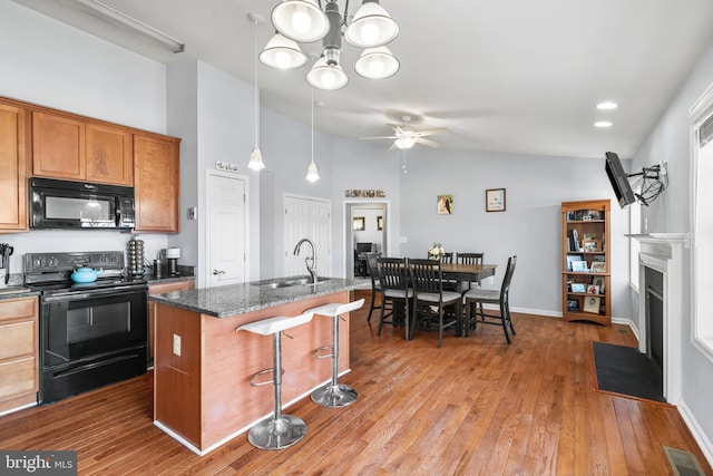 kitchen with visible vents, a fireplace with flush hearth, a kitchen breakfast bar, black appliances, and a sink