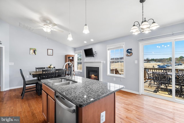 kitchen with dishwasher, lofted ceiling, brown cabinetry, a glass covered fireplace, and a sink