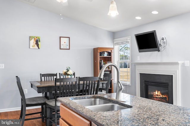 kitchen with baseboards, dark wood finished floors, dark stone countertops, a glass covered fireplace, and a sink