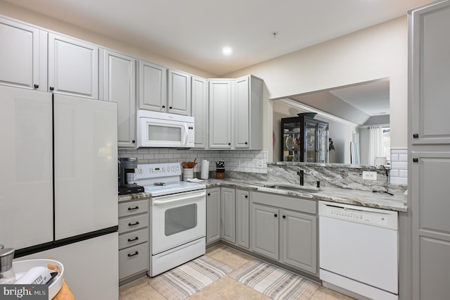 kitchen featuring tasteful backsplash, light tile patterned floors, gray cabinets, white appliances, and a sink