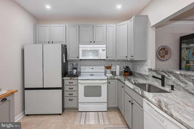 kitchen with a sink, recessed lighting, white appliances, decorative backsplash, and light stone countertops