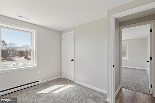 unfurnished bedroom featuring a baseboard heating unit, carpet flooring, baseboards, and visible vents