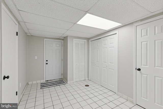 foyer entrance with light tile patterned flooring, a paneled ceiling, and baseboards