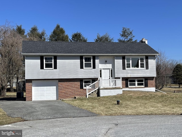 split foyer home featuring an attached garage, brick siding, driveway, and a chimney