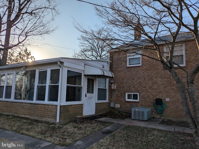 view of front of home featuring brick siding, central AC unit, a chimney, and a sunroom