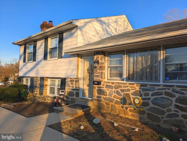 split level home with stone siding and a chimney