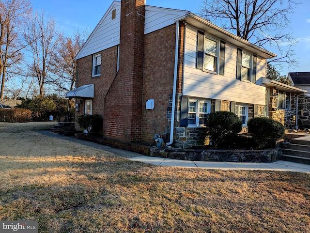 view of home's exterior featuring brick siding, a lawn, and a chimney