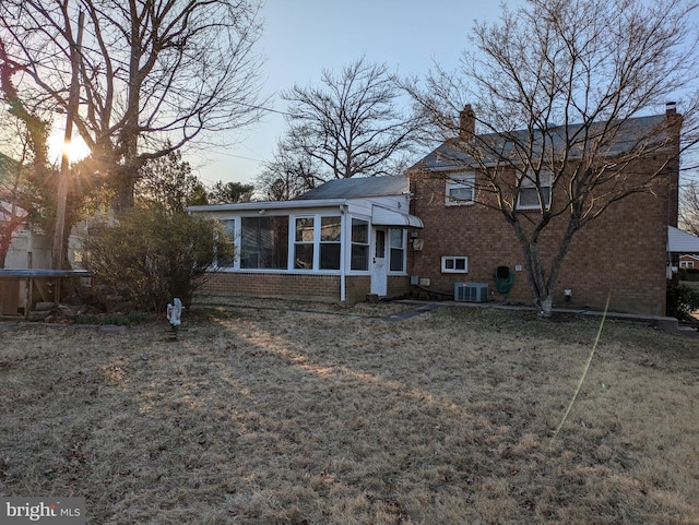 rear view of house featuring a trampoline, cooling unit, a sunroom, brick siding, and a chimney