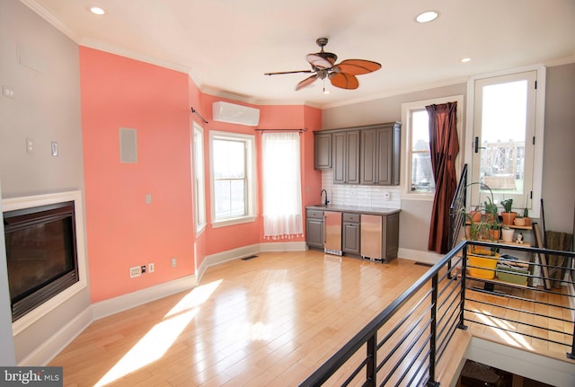 kitchen with backsplash, crown molding, baseboards, light wood-style flooring, and a glass covered fireplace