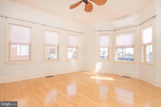 spare room featuring a wall unit AC, a healthy amount of sunlight, visible vents, and light wood finished floors