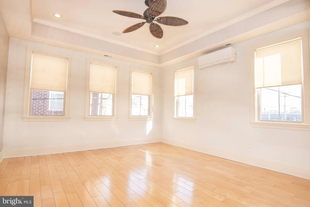 spare room with baseboards, a raised ceiling, light wood-style floors, and a wall unit AC