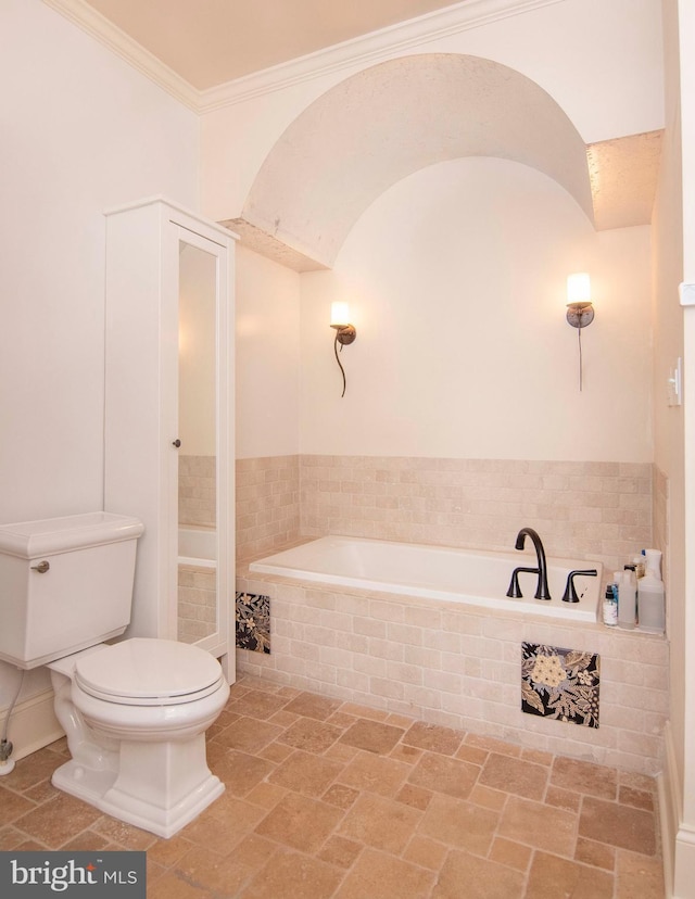 bathroom with toilet, stone finish flooring, a bath, and ornamental molding