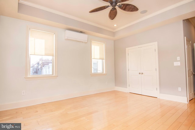 spare room featuring light wood finished floors, crown molding, a wall mounted AC, and a tray ceiling