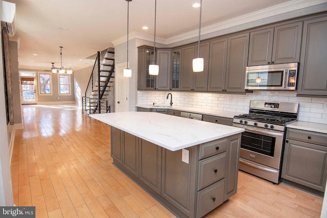 kitchen with a kitchen island, gray cabinets, stainless steel appliances, light wood-type flooring, and backsplash