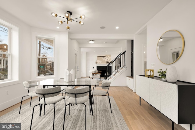 dining area featuring light wood-type flooring, stairway, baseboards, and a notable chandelier