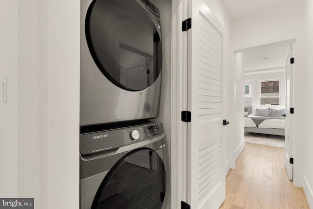 clothes washing area featuring laundry area, light wood-style floors, and stacked washer / drying machine