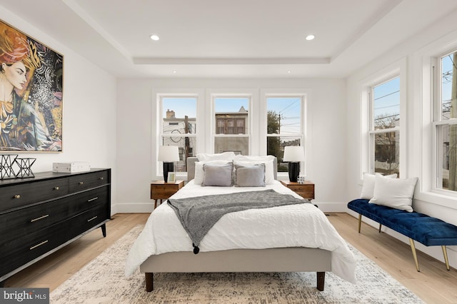 bedroom featuring a tray ceiling, multiple windows, and light wood finished floors