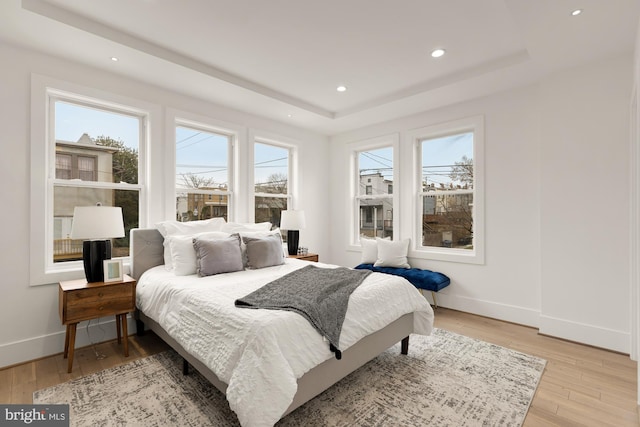 bedroom with a tray ceiling, light wood-type flooring, baseboards, and recessed lighting