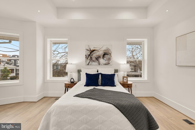 bedroom featuring multiple windows, a raised ceiling, baseboards, and light wood-style flooring