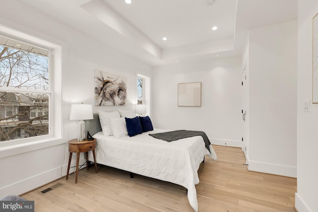 bedroom with baseboards, visible vents, a tray ceiling, light wood-style flooring, and recessed lighting