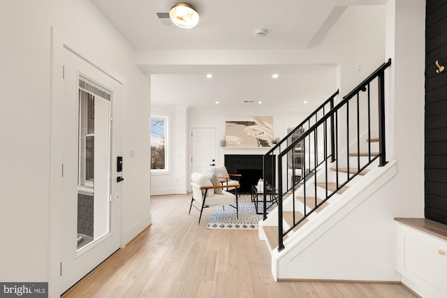 entrance foyer featuring recessed lighting, light wood-type flooring, a brick fireplace, and stairs